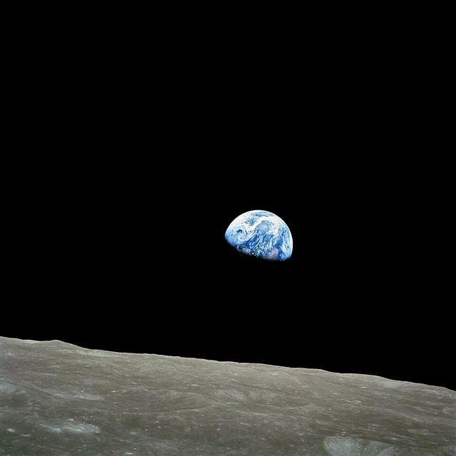 Photograph from lunar orbit: a small, partly lit blue and white Earth above the grey lunar horizon in a black sky.